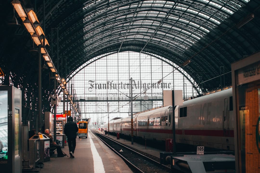 People stand and walk in a train station concourse during the day.